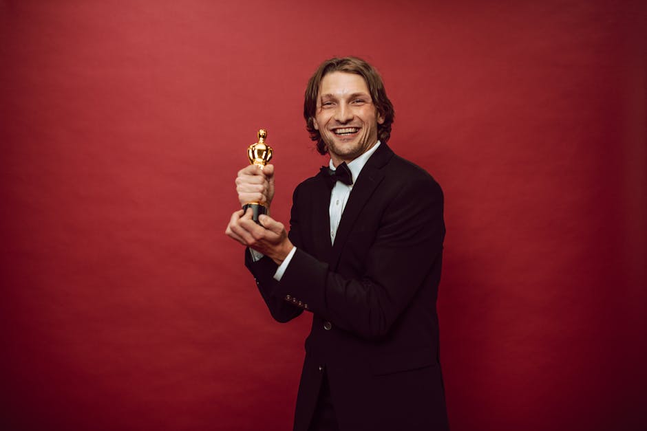 Smiling man in a tuxedo holding a trophy against a red background